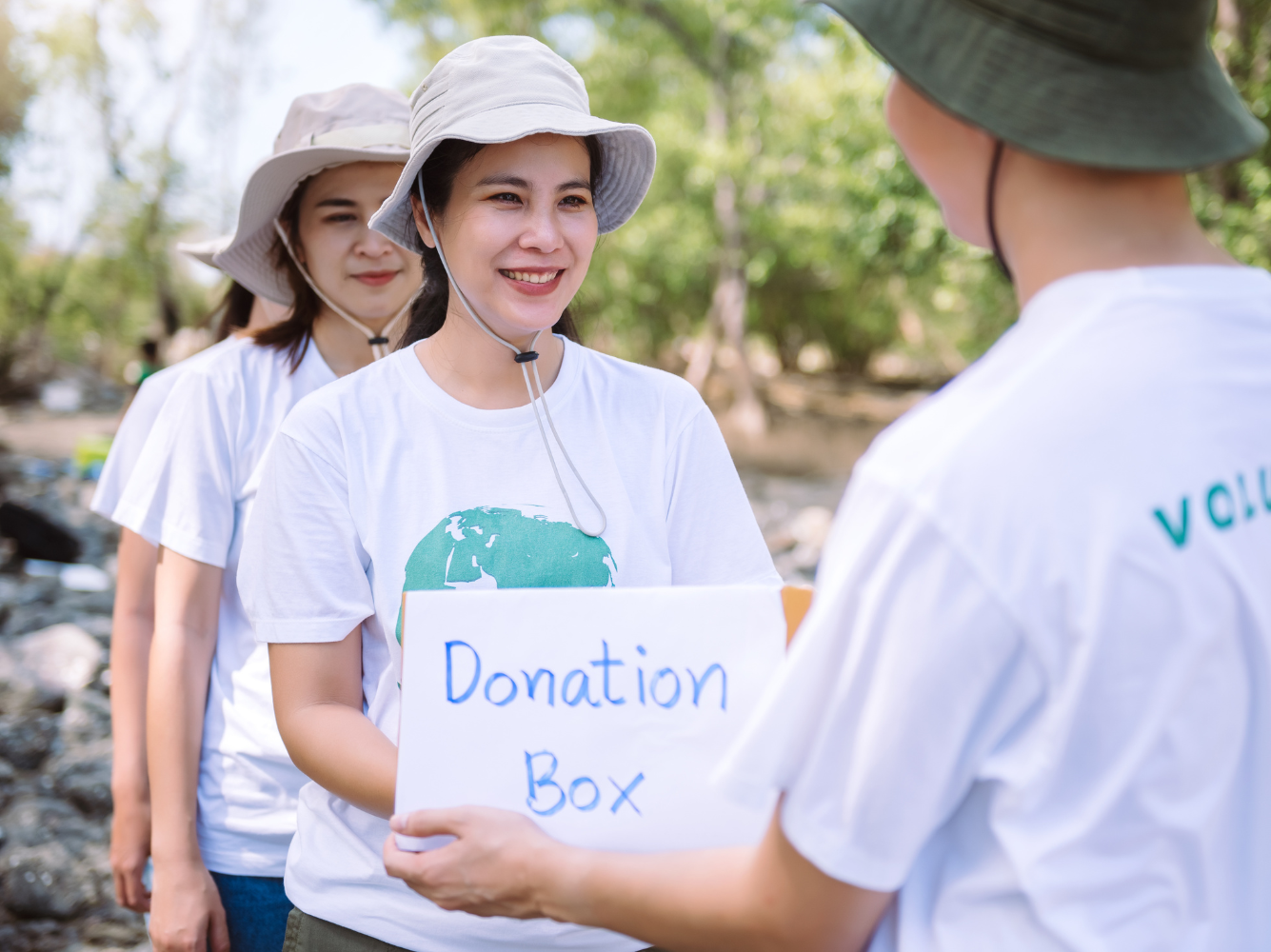 Group of volunteers smiling and handing over a donation box outdoors, representing generosity, teamwork, and the spirit of Giving Tuesday marketing.
