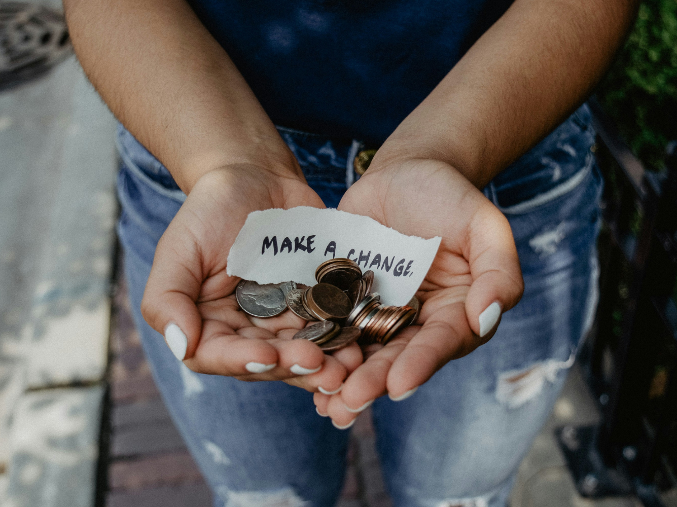Close-up of hands holding coins and a paper that says “Make a Change,” symbolizing generosity and small acts of kindness on Giving Tuesday.