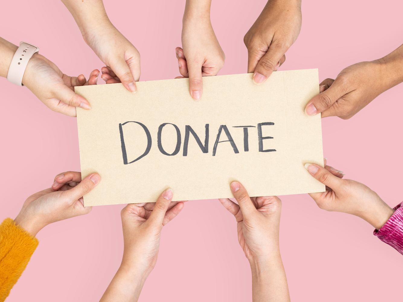 Group of diverse hands holding a cardboard sign that says “Donate,” representing collective generosity and collaboration in Giving Tuesday marketing campaigns.