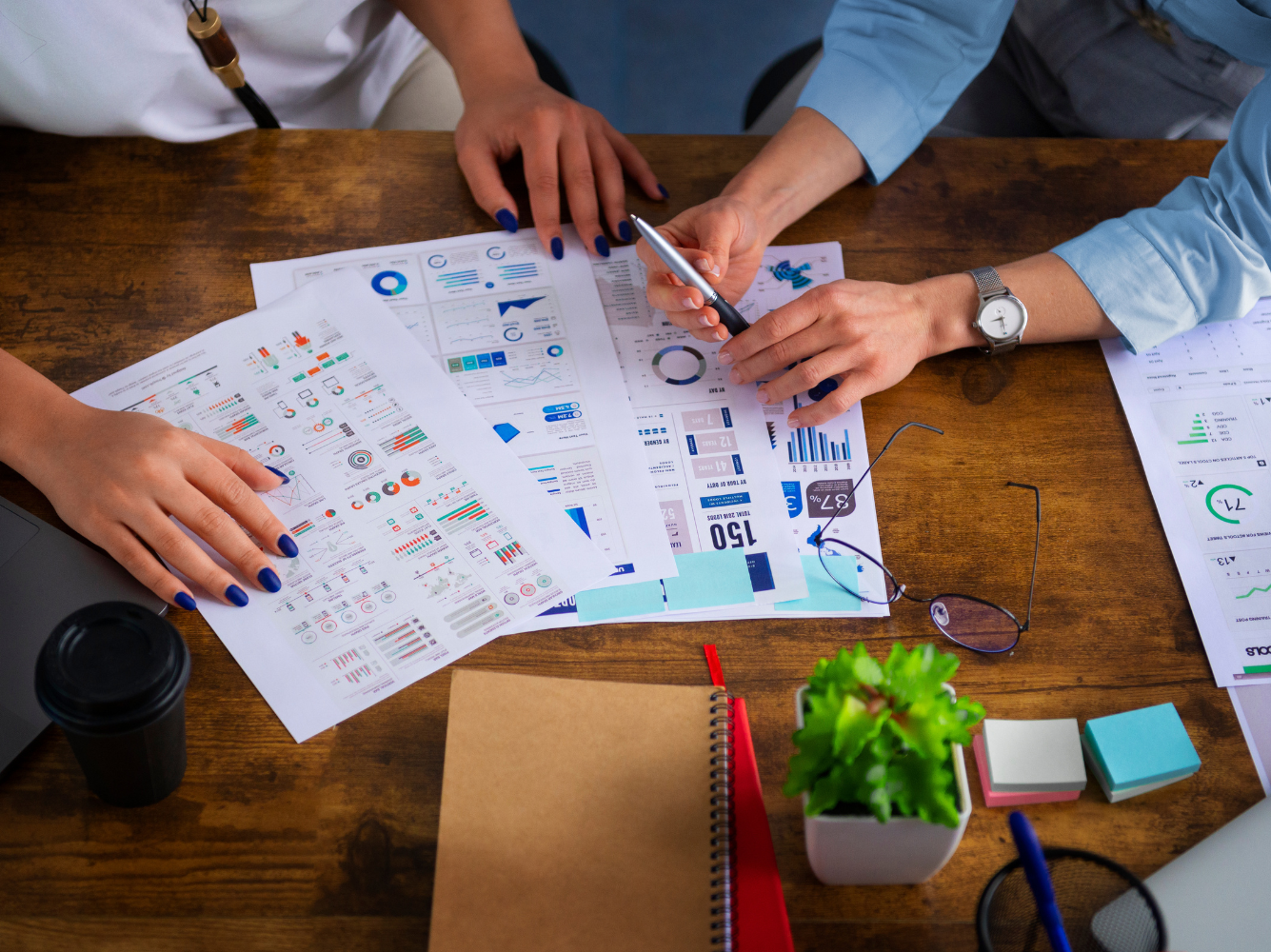 two marketers collaborating at a wooden desk, analyzing charts and data sheets for a Giving Tuesday marketing campaign, surrounded by laptops, notebooks, and colorful office supplies
